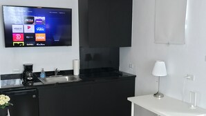 Una cucina moderna con un piano di lavoro nero, un tavolo bianco e una TV a muro che mostra servizi di streaming.
