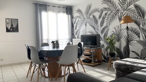Uma sala de estar moderna com área de jantar, com uma mesa redonda, cadeiras, televisão de tela plana e um sofá.