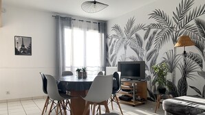 A modern living room with a dining area, featuring a flat-screen TV, a sofa, and a dining table with chairs. - Disneyland Paris 3 minutes away, sleeps 8, 2 bedrooms. (Chessy)