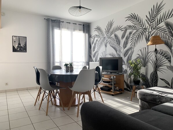 Uma sala de estar moderna com área de jantar, apresentando uma televisão de tela plana, um sofá e uma mesa de jantar com cadeiras.