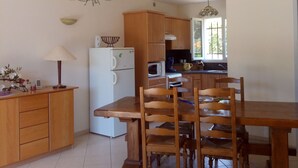 Una cocina amplia con armarios de madera, una mesa de comedor y sillas. Hay una araña colgando sobre la mesa y un microondas en la encimera.