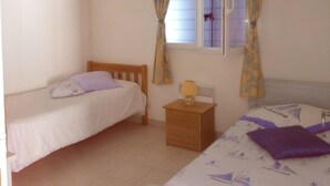 Un dormitorio con dos camas individuales, una mesita de noche, una ventana con cortinas y una lámpara colgante.