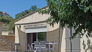 Un patio exterior moderno con una mesa, sillas, un muro de piedra y un ventanal grande.