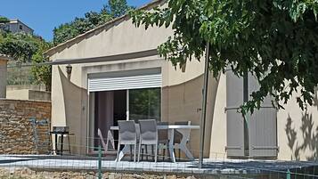 Une terrasse extérieure moderne, dotée d’une table et de chaises, d’un mur en pierre et d’une grande fenêtre.