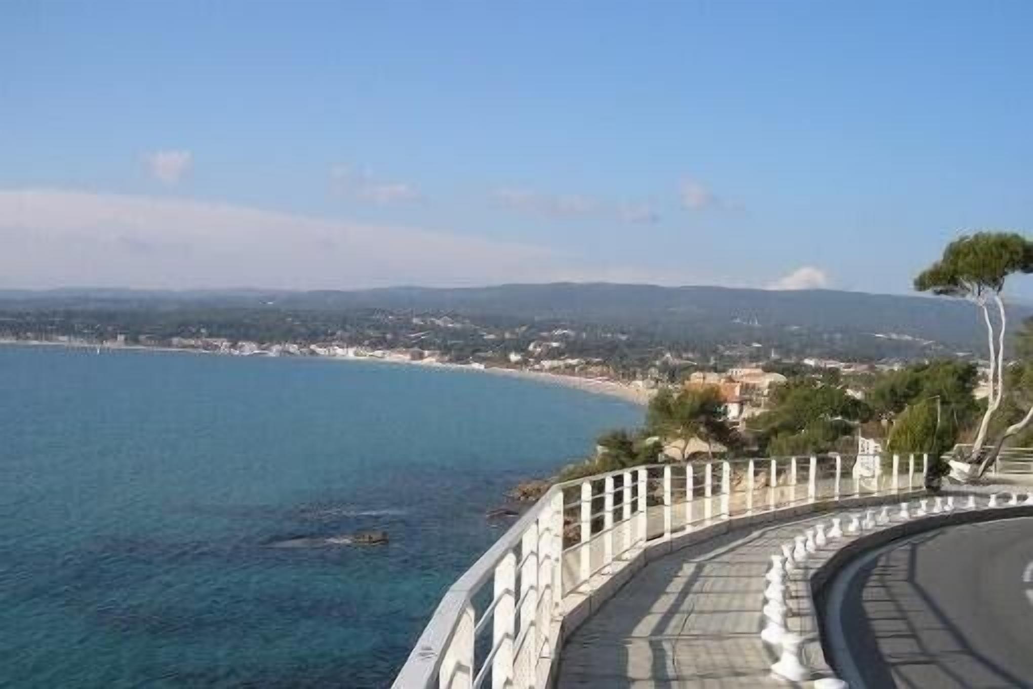 A coastal road with a guardrail, overlooking a beach and a distant town.