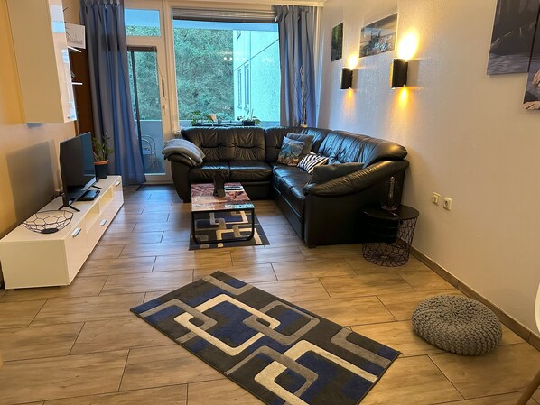 Una sala de estar moderna con un sofá de cuero, una mesa de centro, un televisor y una alfombra estampada.