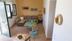 Una sala de estar con un sofá, una mesa de comedor con sillas y una mesita con un jarrón y flores.