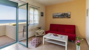 Un balcón con puerta de cristal, un sofá rojo, una mesita con un jarrón y un cuadro en la pared.