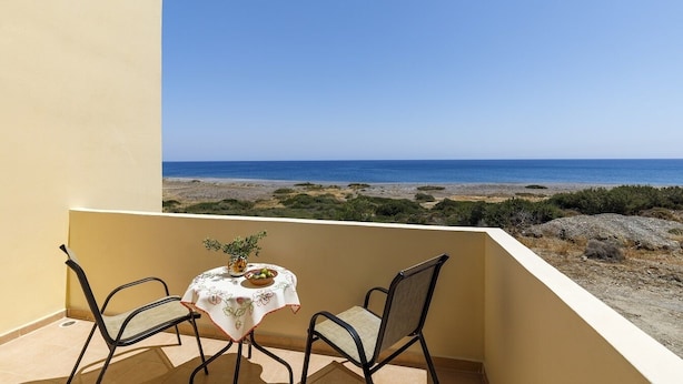 Balcón con mesa y sillas, con vista a una playa y terreno rocoso.