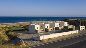 Complejo de edificios costeros con varias estructuras, una carretera pavimentada en primer plano y una vista despejada del mar al fondo.