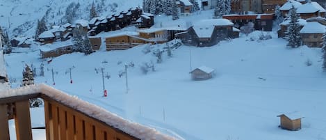 A snowy mountain landscape with a wooden balcony overlooking a snow-covered village and a mountain.