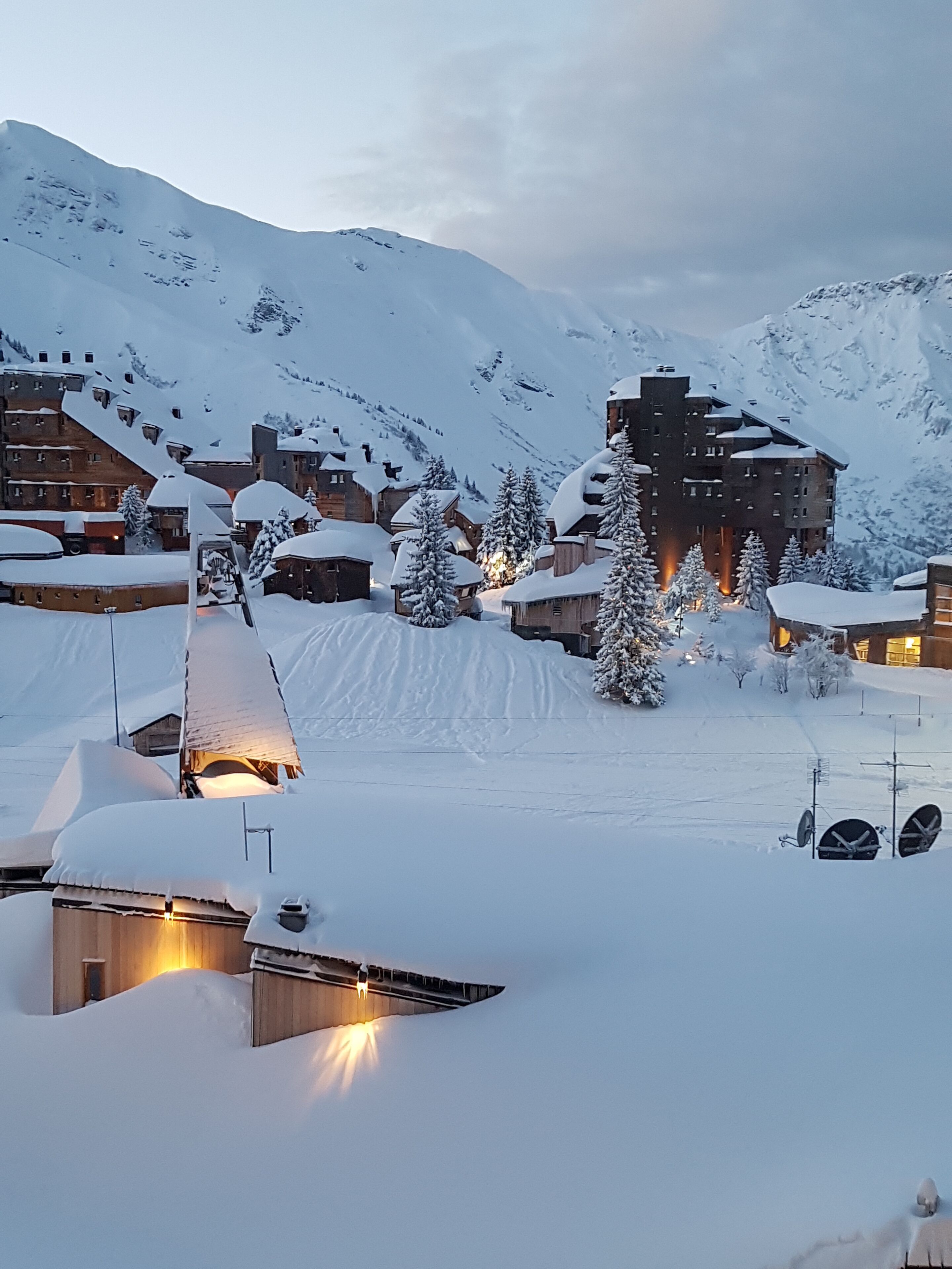 A snow-covered mountain resort with wooden buildings and a large hotel in the background.
