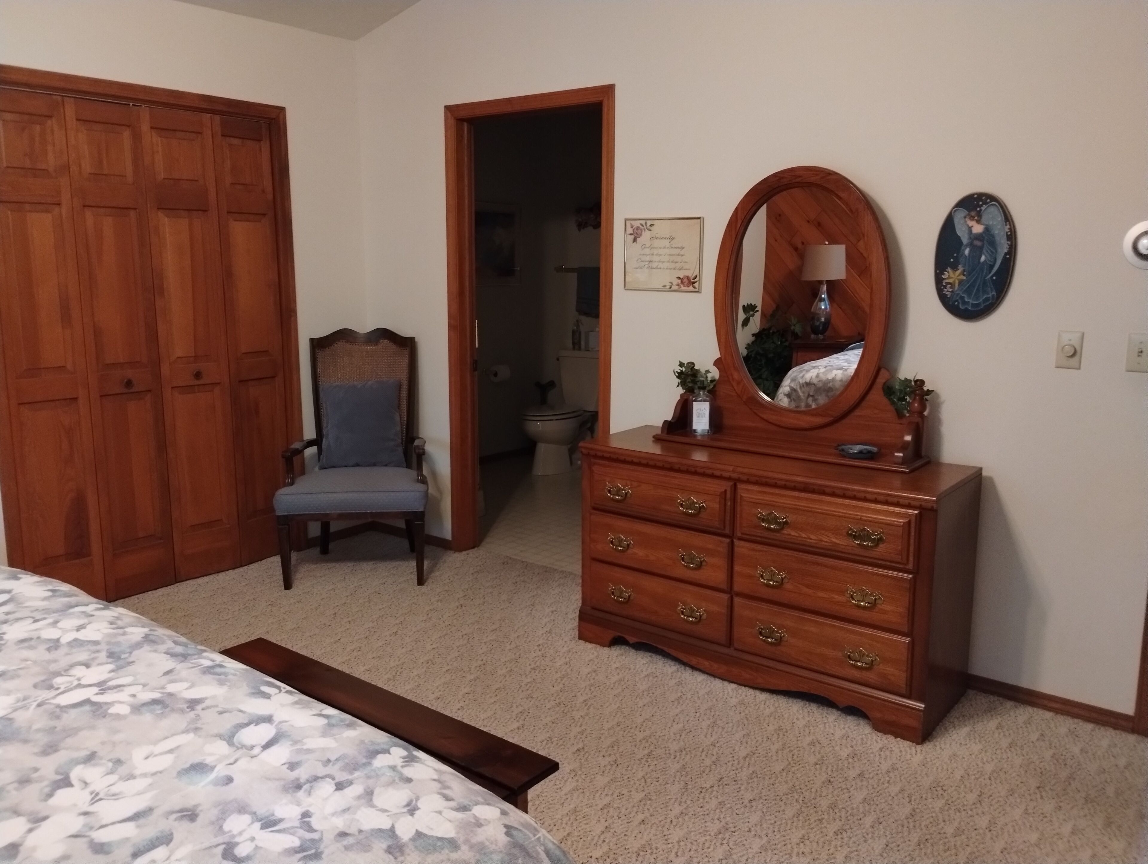 A bedroom with a bed, a wooden dresser with a mirror, a chair, and a wardrobe.