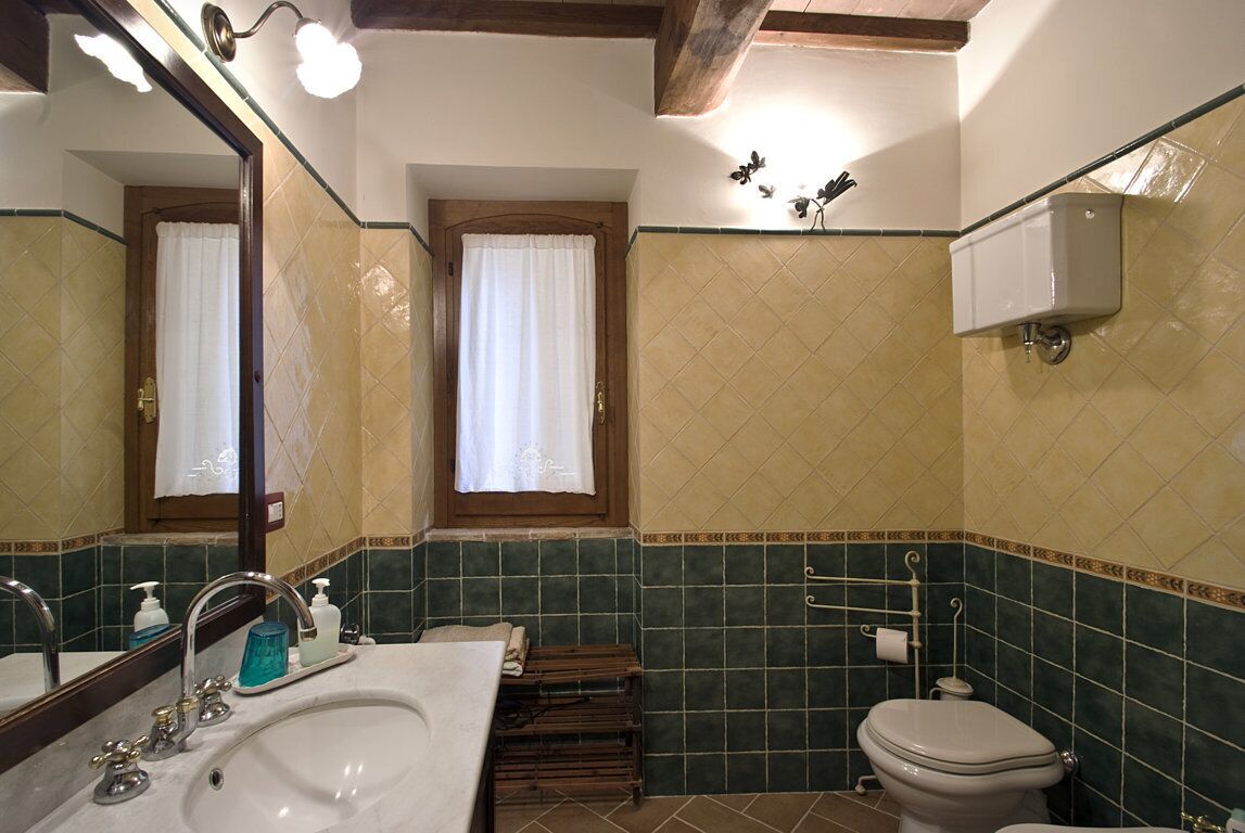 A bathroom with a sink, mirror, toilet, and a window with curtains.