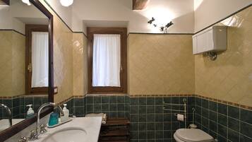 A bathroom with a sink, mirror, toilet, and a window with curtains.