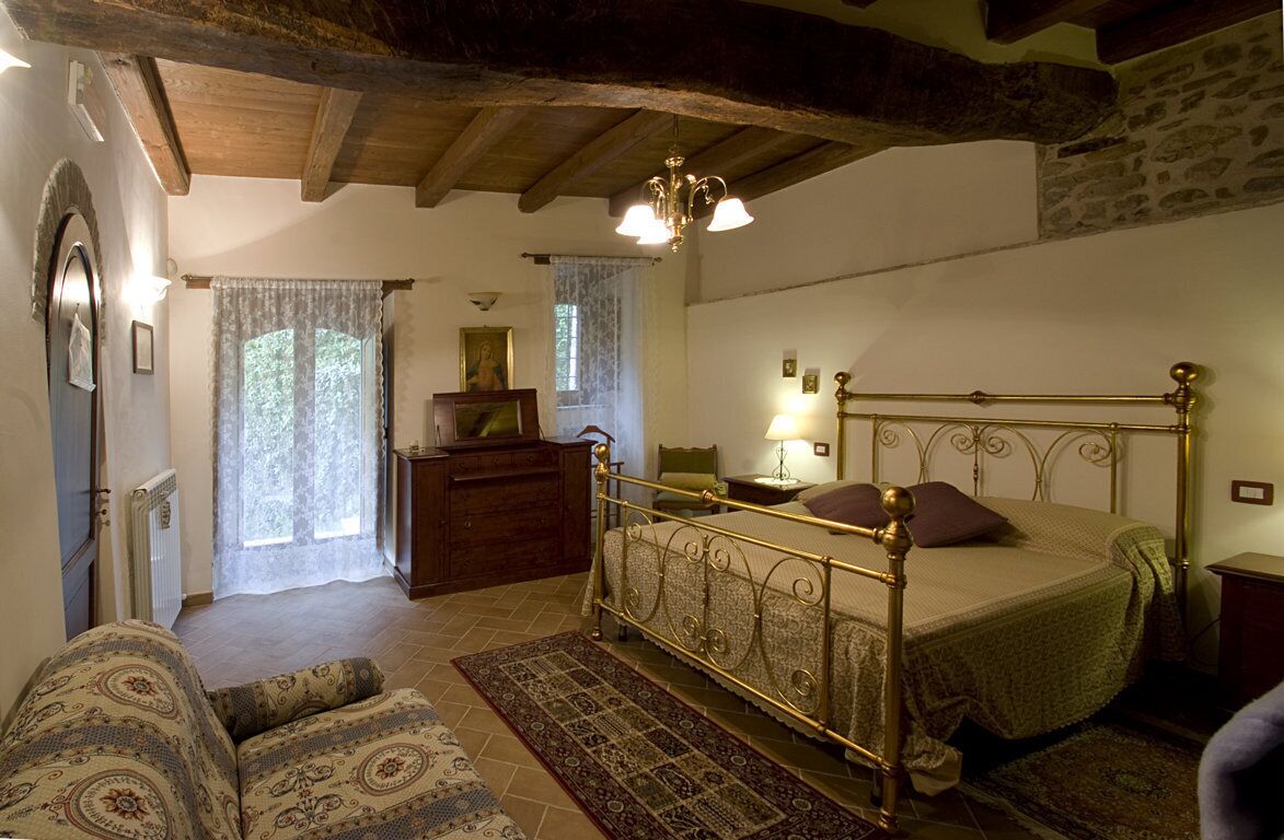 A bedroom with a four-poster bed, a wooden ceiling, a radiator, a dresser, and a window with lace curtains.