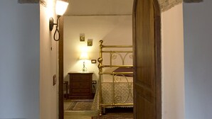 Un couloir étroit, surmonté d’une arche en briques, mène à une chambre.