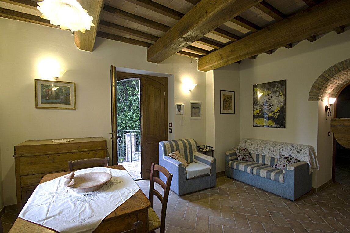 A cozy living room with a wooden table, a sofa, and a chair. There is a door leading to an outdoor area.