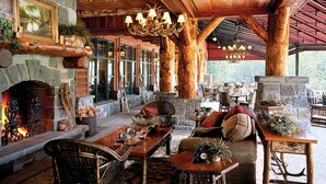 A cozy lodge interior with a stone fireplace, wooden furniture, and a large chandelier.