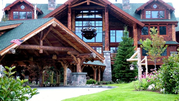 A large, rustic lodge with a prominent stone chimney, a covered porch, and a well-maintained garden.