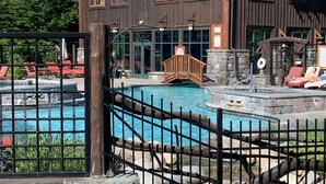 A pool area with a wooden fence, lounge chairs, and a building with large windows in the background.