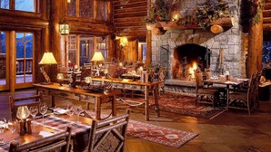 A cozy, rustic interior with wooden furniture, a stone fireplace, and a view of the outdoors.
