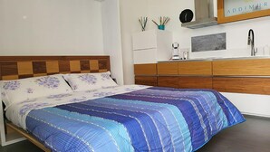 A modern bedroom with a wooden headboard, a bed with floral and striped bedding, a white dresser, and a wall-mounted mirror. - Studio apartment two beds (Marina di Palma)