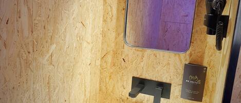 A bathroom with a wooden wall, a white sink, a mirror, and a black towel dispenser.