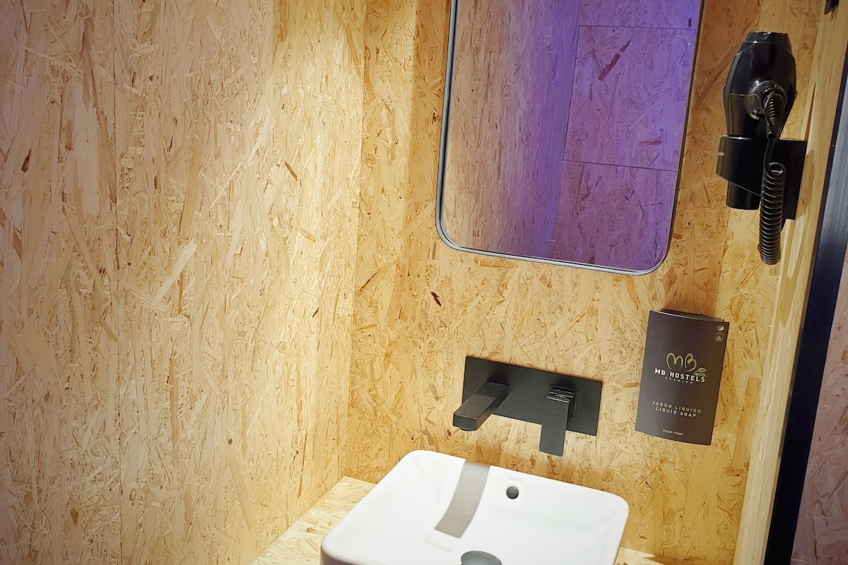 A bathroom with a wooden wall, a white sink, a mirror, and a black hairdryer.
