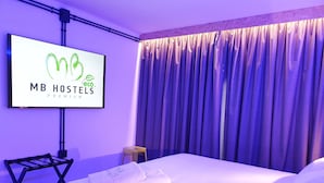 A hotel room with a bed, a TV mounted on the wall, and a curtain. - MB Hostels Premium Eco (Nerja)