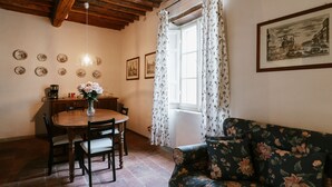 Zona pranzo con tavolo e sedie in legno, un divano floreale e una finestra con tende.