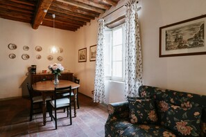 Un coin repas avec une table et des chaises en bois, un canapé à motifs floraux et une fenêtre avec des rideaux.