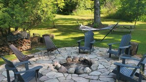 A stone fire pit surrounded by Adirondack chairs, a hammock, and a stone wall.