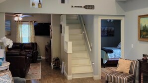 A spacious living area with a high ceiling, a staircase leading to a bedroom, and a cozy seating area with a fireplace.