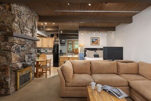 A cozy living room with a stone wall, a fireplace, a sofa, and a coffee table. - Aspenwood K2 - Ski, Soak, Relax | Cozy Mountain Stay, Walk to Slopes (Snowmass Village)