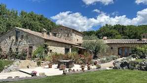 Una casa in pietra con tetto in tegole, circondata da un giardino con piante in vaso e un patio.