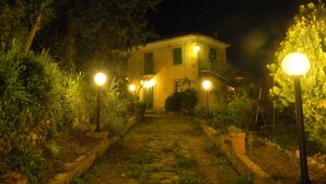 A house with a paved pathway leading to the entrance, surrounded by greenery and illuminated by street lamps. - Nunziata House (Mineo)
