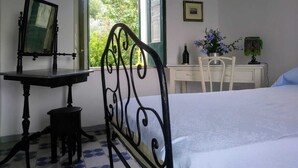 A bedroom with a bed, a desk, a chair, a mirror, and a window with a view of greenery. - Nunziata House (Mineo)