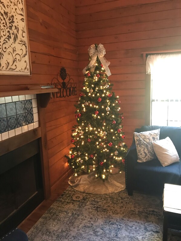 Une pièce chaleureuse avec un décor en bois, un sapin de Noël décoré de guirlandes lumineuses et d’ornements, une cheminée et un canapé bleu agrémenté de coussins.