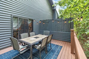 Une terrasse avec une table et des chaises, une plateforme en bois et une vue sur une maison recouverte de bardage.