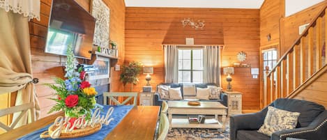 A cozy cabin interior with a wooden floor, a sofa, a dining table, and a staircase.