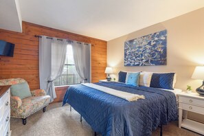 Une chambre à coucher avec un lit, une chaise, une table de chevet, une lampe et un tableau au mur.