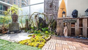Um jardim com uma estátua de Buda, bambu e uma placa de madeira com a inscrição 'Quem planta um jardim planta felicidade'.