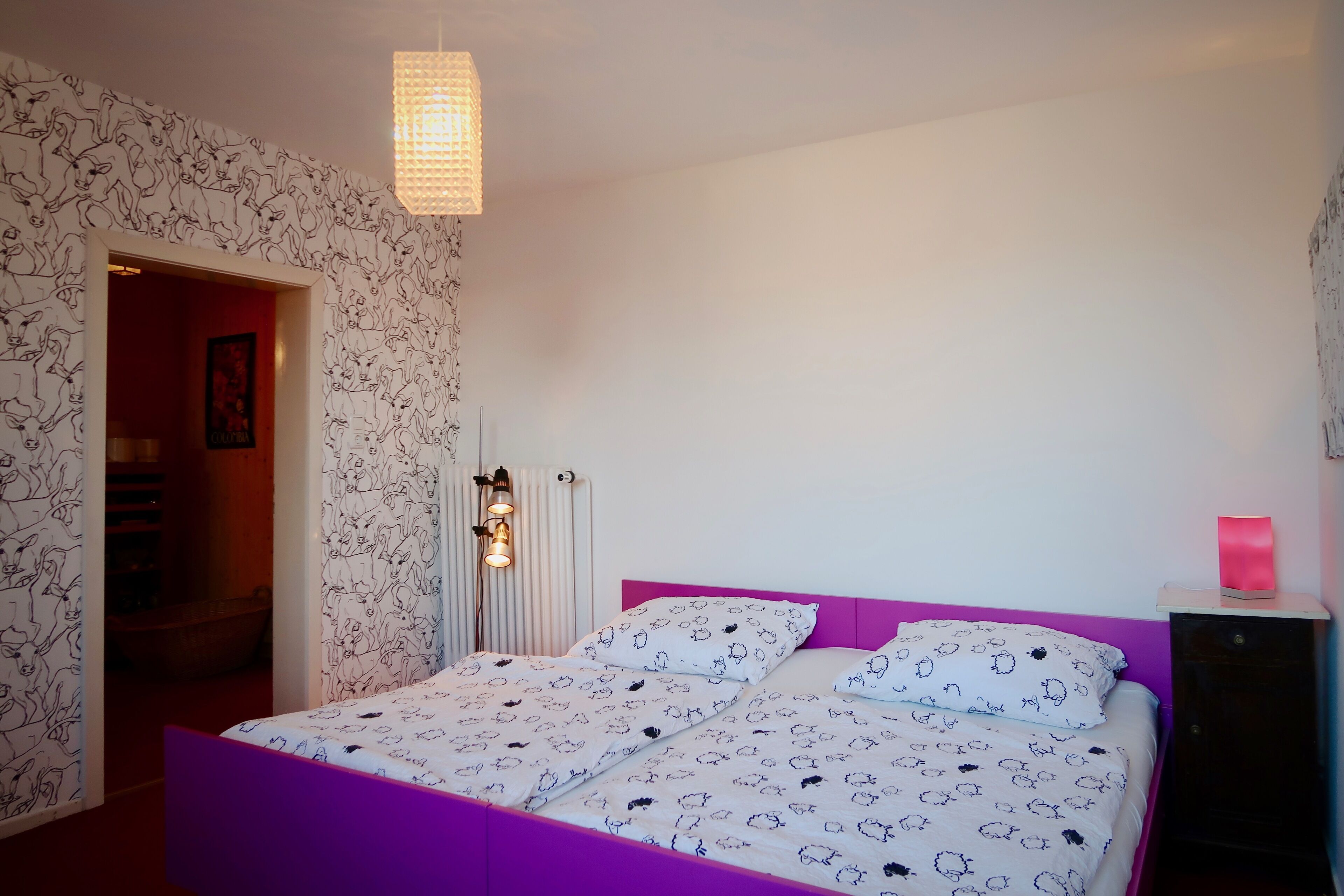 A bedroom with a bed, a nightstand, a lamp, and a door leading to another room.