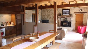 Una cocina rústica con vigas de madera, pared de piedra, chimenea y comedor con mesa y bancos de madera.