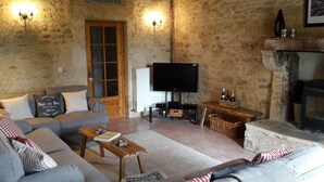 Una sala de estar acogedora con una pared de piedra, una puerta de madera, un televisor y una chimenea.