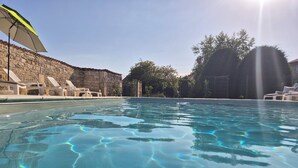 Una piscina cristalina con un muro de piedra y sillones de descanso al fondo.
