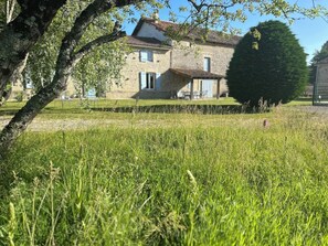A stone house with a well-maintained lawn and a large tree in the foreground.