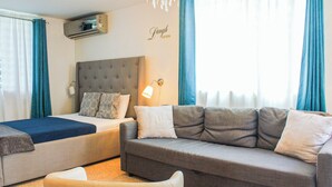 A hotel room with a bed, a sofa, a wall-mounted air conditioner, a wall lamp, and a window with curtains.