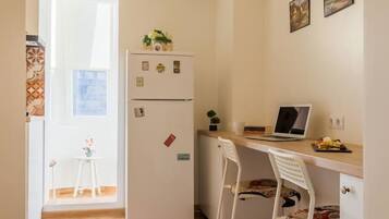 A compact kitchen with a refrigerator, a dining table with chairs, and a laptop on the table.